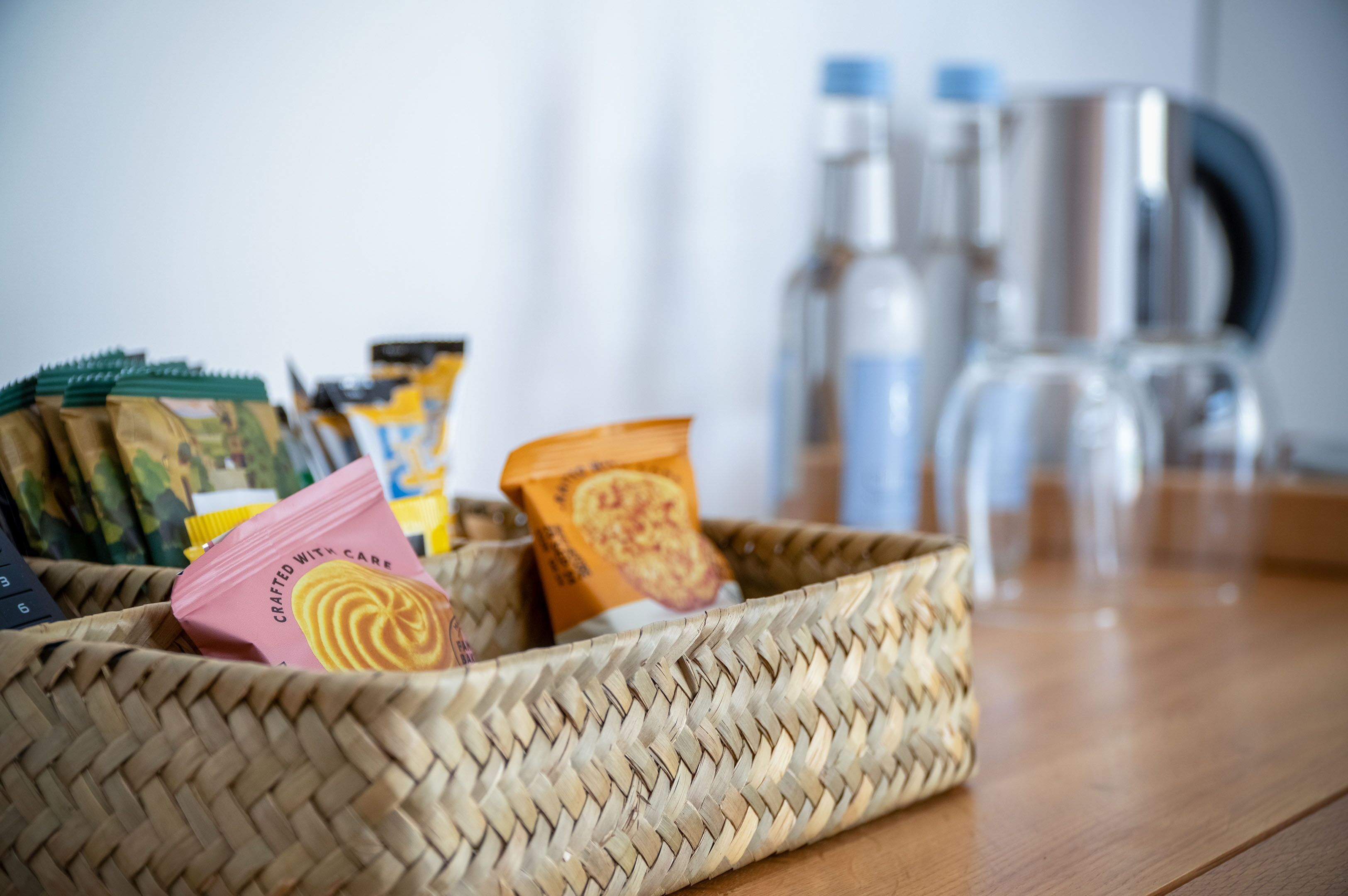 A woven basket containing various packaged snacks and a coffee maker on a wooden table.
