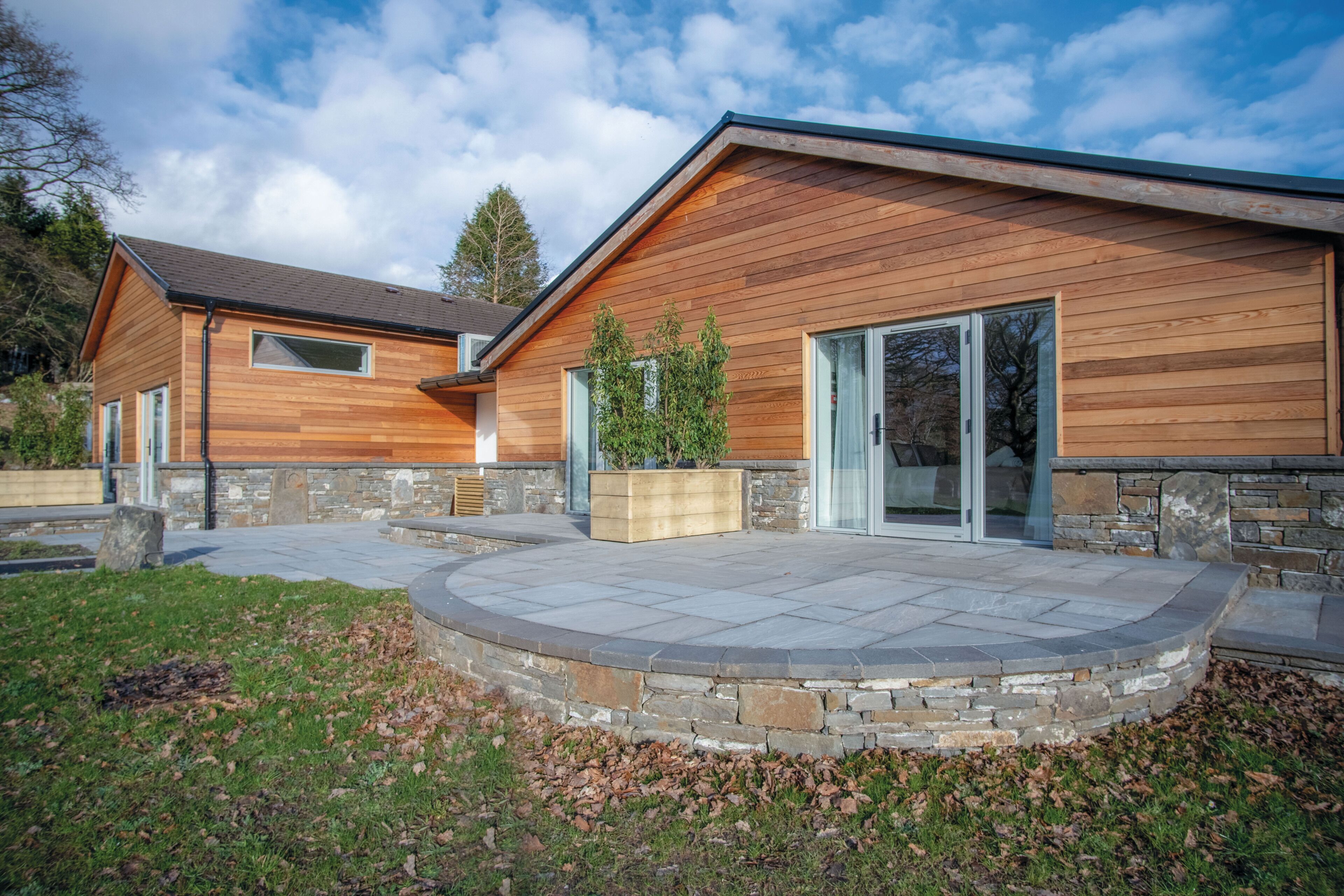 Une maison moderne avec des fondations en pierre, un revêtement extérieur en bois et une terrasse en pierre.