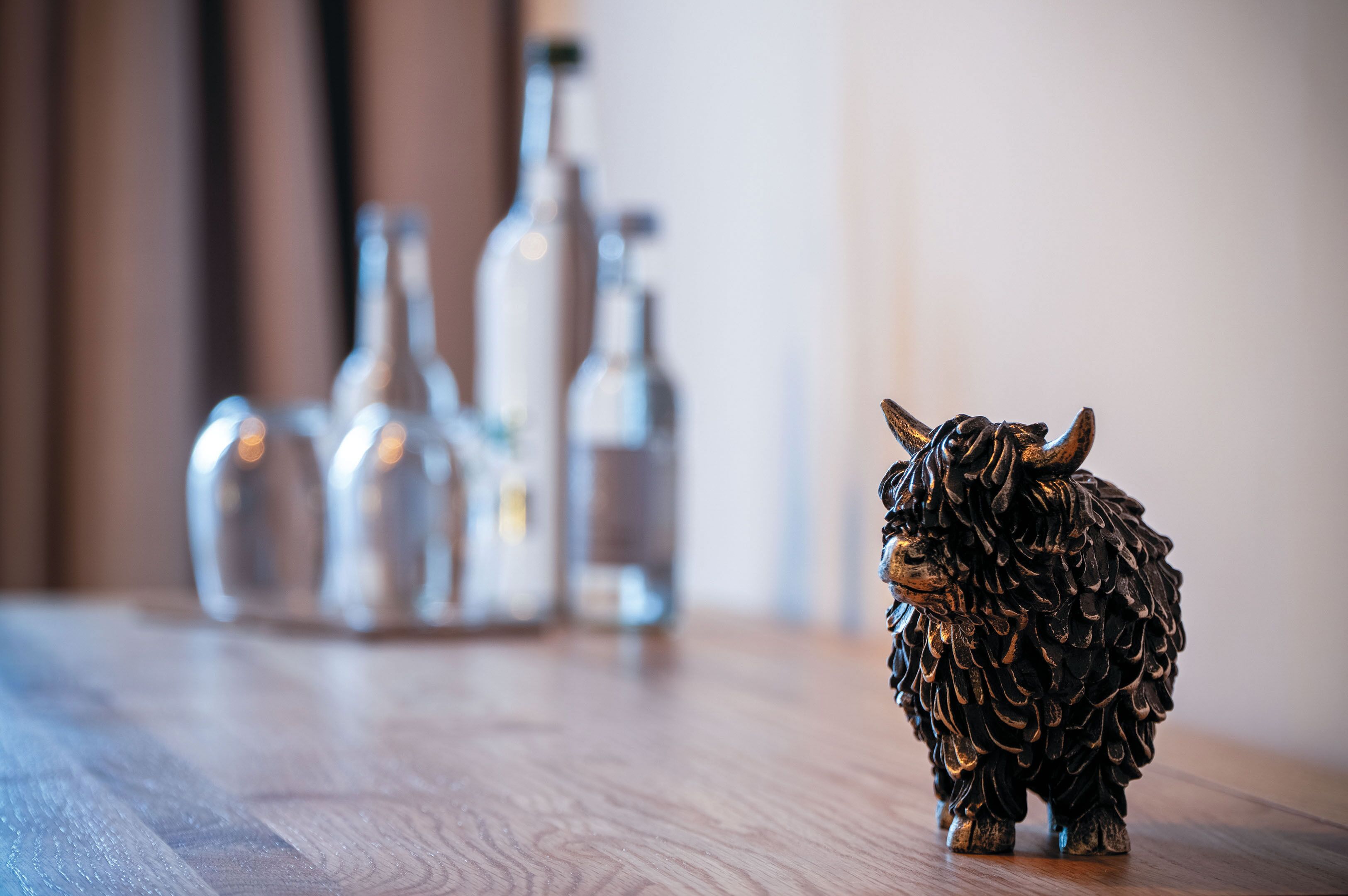 Une figurine de taureau décorative posée sur une surface en bois, avec des bouteilles floues en arrière-plan.