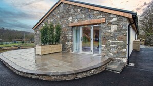 A stone building with a wooden roof, large glass doors, and a paved patio area. - The Sleeping Giant - Pen Y Cae Inn (Swansea)