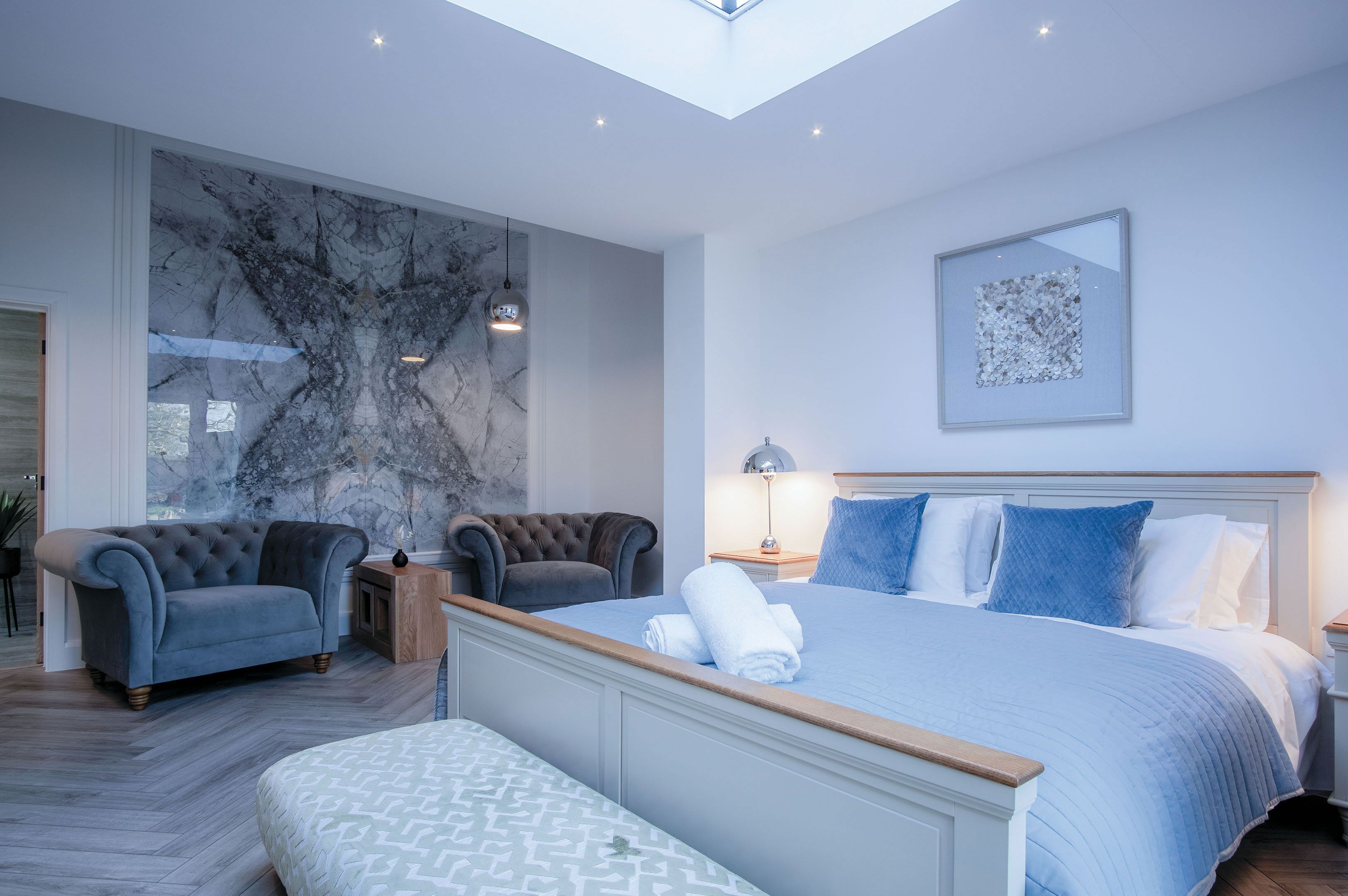 Ein modernes Schlafzimmer mit einem großen Bett, einem gepolsterten Sessel, einer Bank und einer Marmorwand.