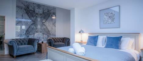 A modern bedroom with a large bed, a tufted armchair, a bench, and a marble wall.