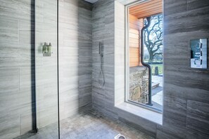 A modern bathroom with a glass-enclosed shower, a built-in window, and a stone wall.