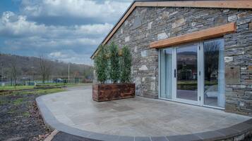 A modern building with stone exterior, large sliding glass doors, and a wooden planter with greenery.