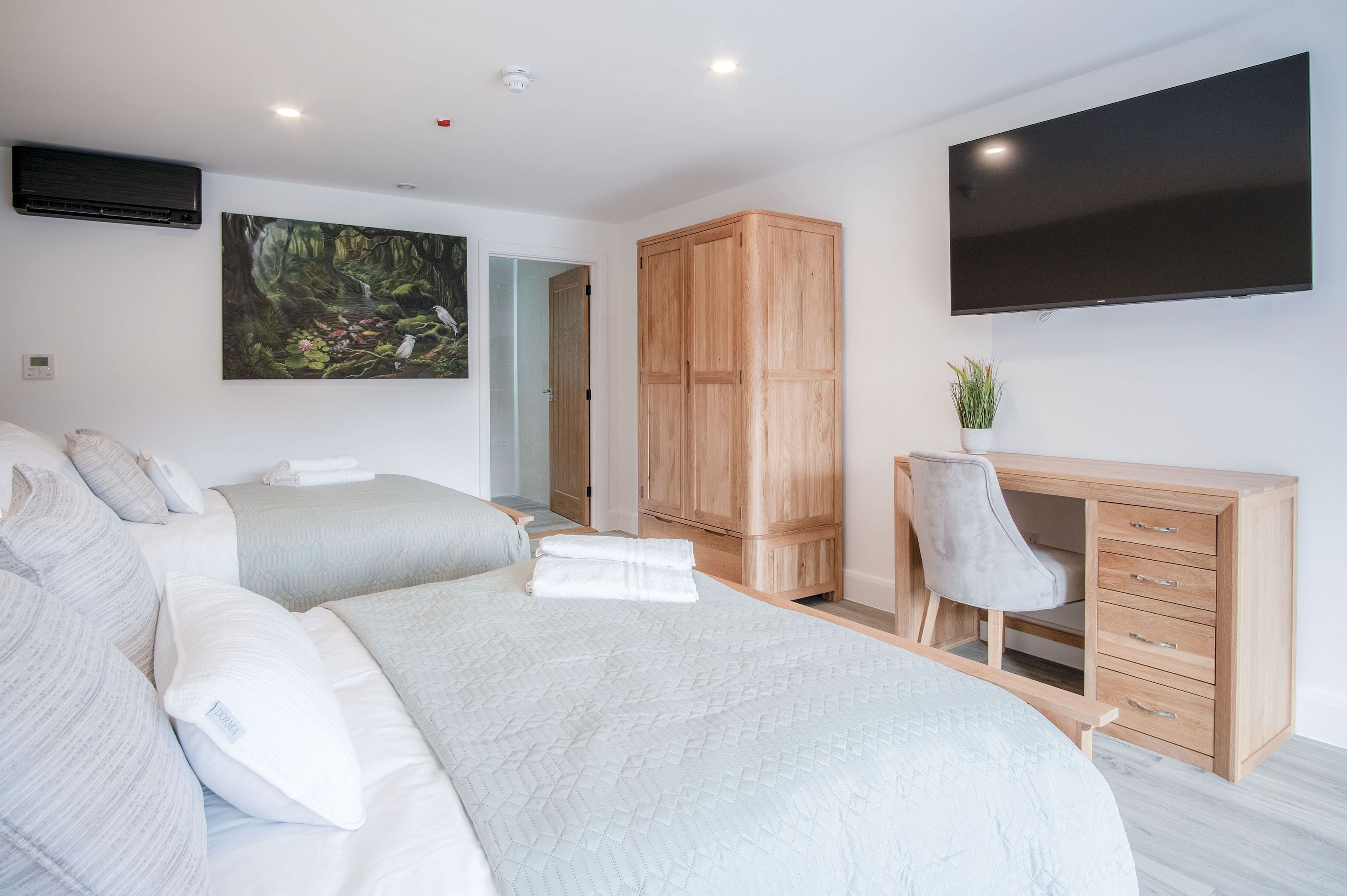 Ein modernes Hotelzimmer mit zwei Betten, einem Holzschrank, einem Schreibtisch mit Stuhl, einem Flachbildfernseher und einem Bild an der Wand.