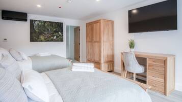 Ein modernes Hotelzimmer mit zwei Betten, einem Holzschrank, einem Schreibtisch mit Stuhl, einem Flachbildfernseher und einem Bild an der Wand.