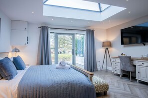 A bedroom with a skylight, a bed with blue bedding, a desk with a chair, and a TV on the wall.