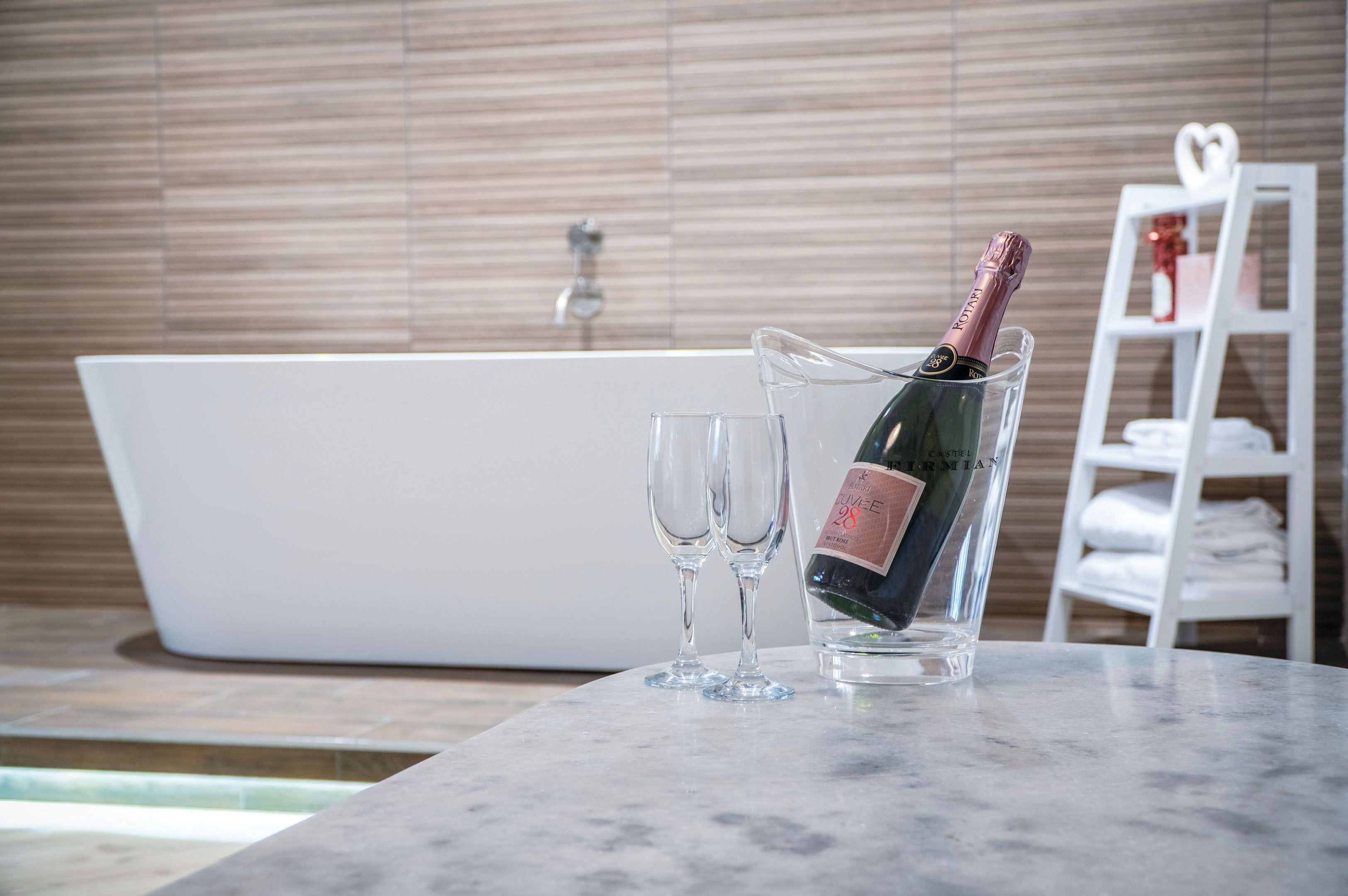 Une salle de bain avec une baignoire, une bouteille de champagne dans un verre et deux verres à vin vides sur un comptoir en marbre.