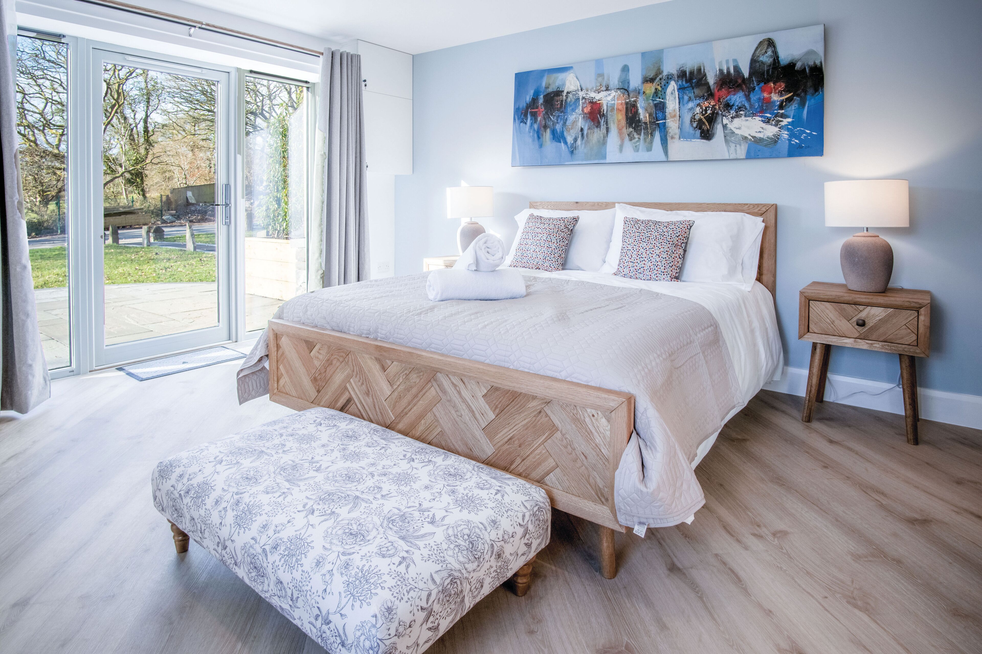 A bedroom with a large bed, a bench, two bedside tables, and a view through a glass door.