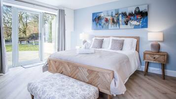 A bedroom with a large bed, a bench, two bedside tables, and a view through a glass door.