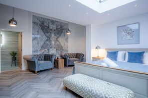 A modern bedroom with a large bed, two armchairs, a small table, and a marble wall.