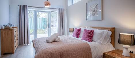 Une chambre à coucher avec un grand lit, une table de chevet en bois, une lampe de chevet et une fenêtre avec des rideaux.