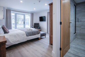 A modern bedroom with a large bed, a chair, a TV, and a wooden wardrobe.