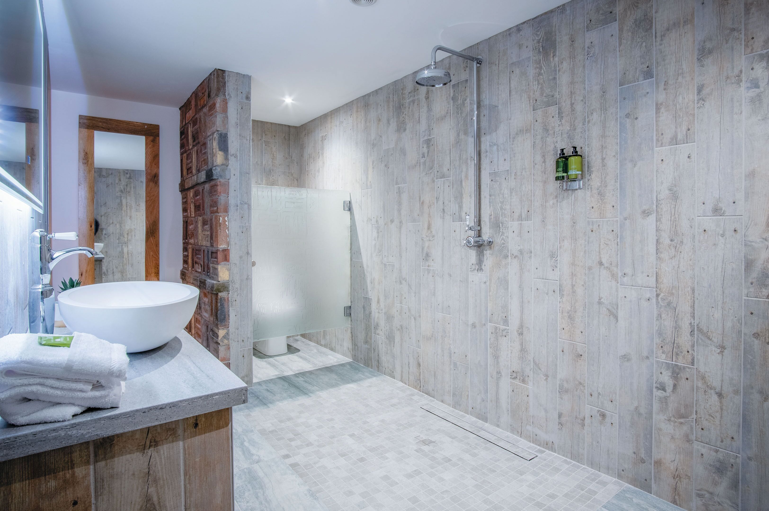 A modern bathroom with a large white sink, a shower with a rain showerhead, and a wooden accent wall.