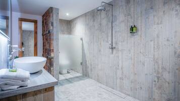 Um banheiro moderno com uma pia grande e branca, chuveiro com ducha de chuva e uma parede de destaque em madeira.