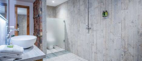 A modern bathroom with a large white sink, a shower with a rain showerhead, and a wooden accent wall.