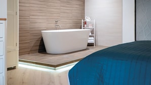 A modern bathroom with a freestanding bathtub, wooden panel walls, and a white shelving unit with toiletries. - The Sleeping Giant - Pen Y Cae Inn (Swansea)