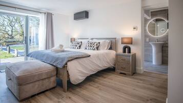 Un dormitorio moderno con una cama grande, mesitas de noche, un banco y un baño con espejo y lavamanos.