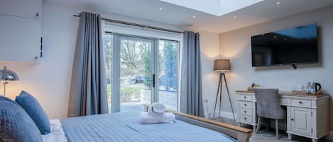 A bedroom with a skylight, a bed with blue bedding, a desk, a chair, and a flat-screen TV.