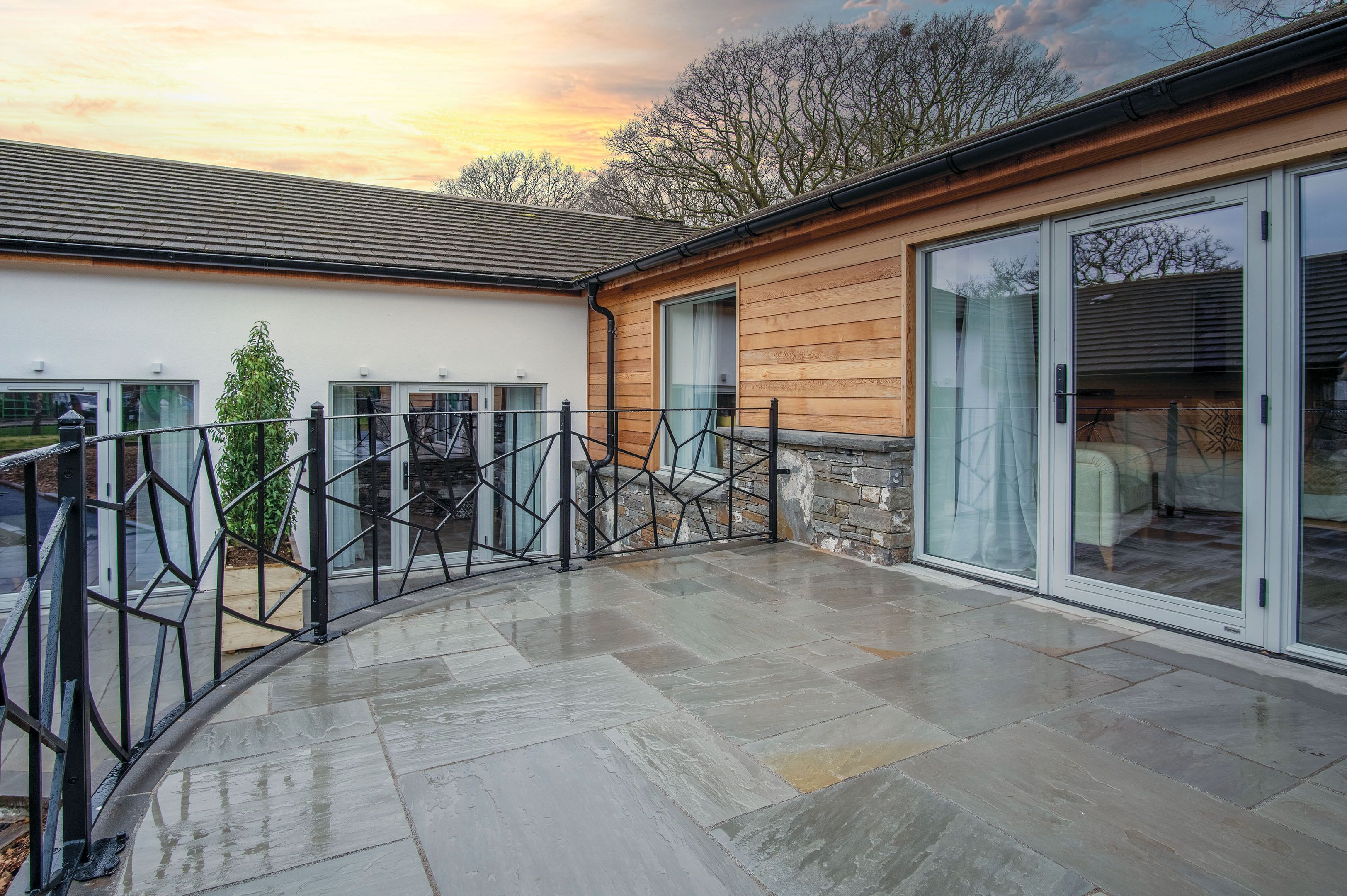 A modern building with a stone facade, large glass doors, and a paved patio area.