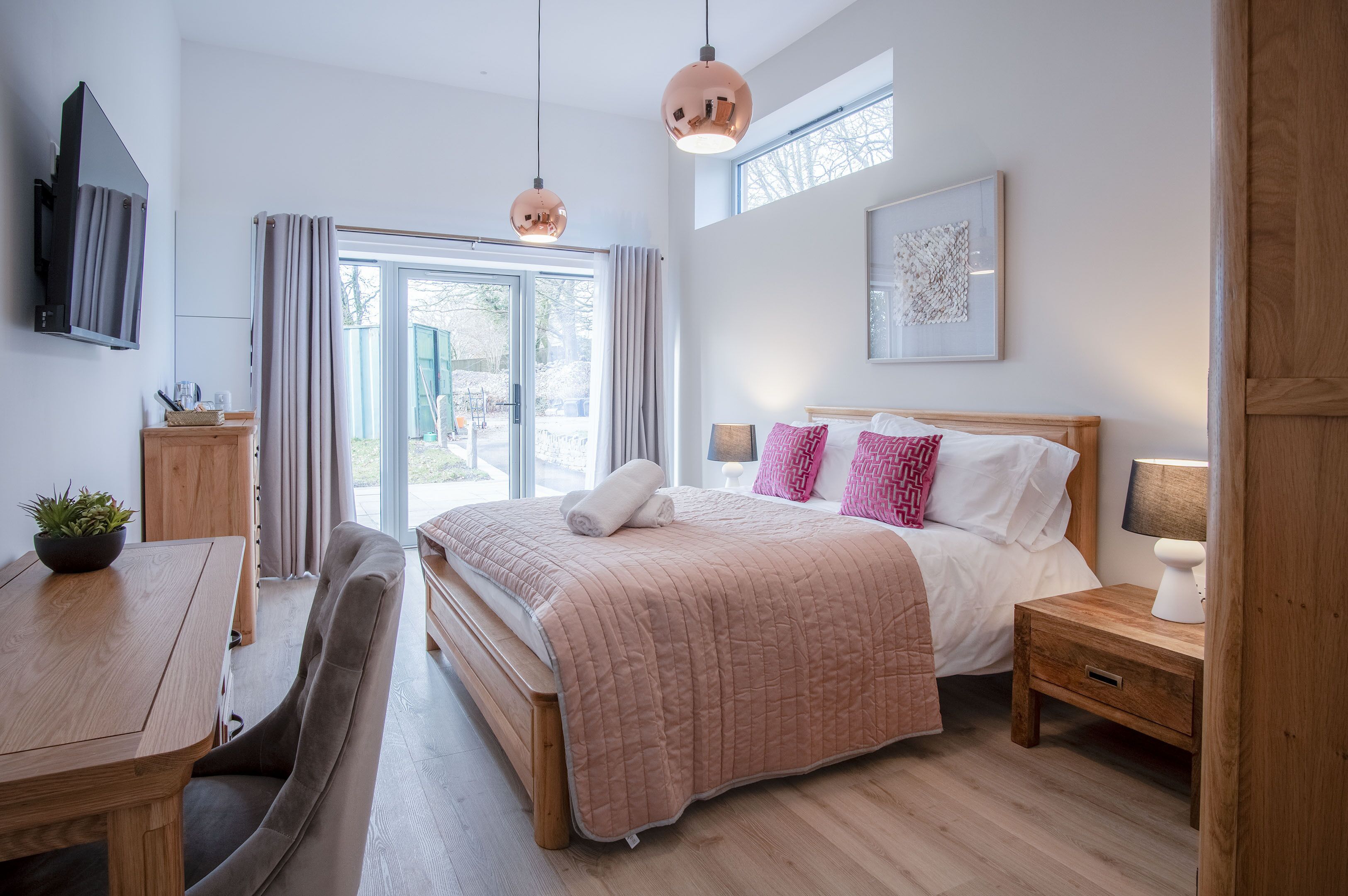 Ein modernes Schlafzimmer mit einem großen Bett, Nachttischen, einem Holztisch und einem an der Wand montierten Fernseher.