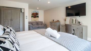 A bedroom with a large bed, a grey sofa, a wooden dresser, a flat-screen TV, and a painting of an elephant.