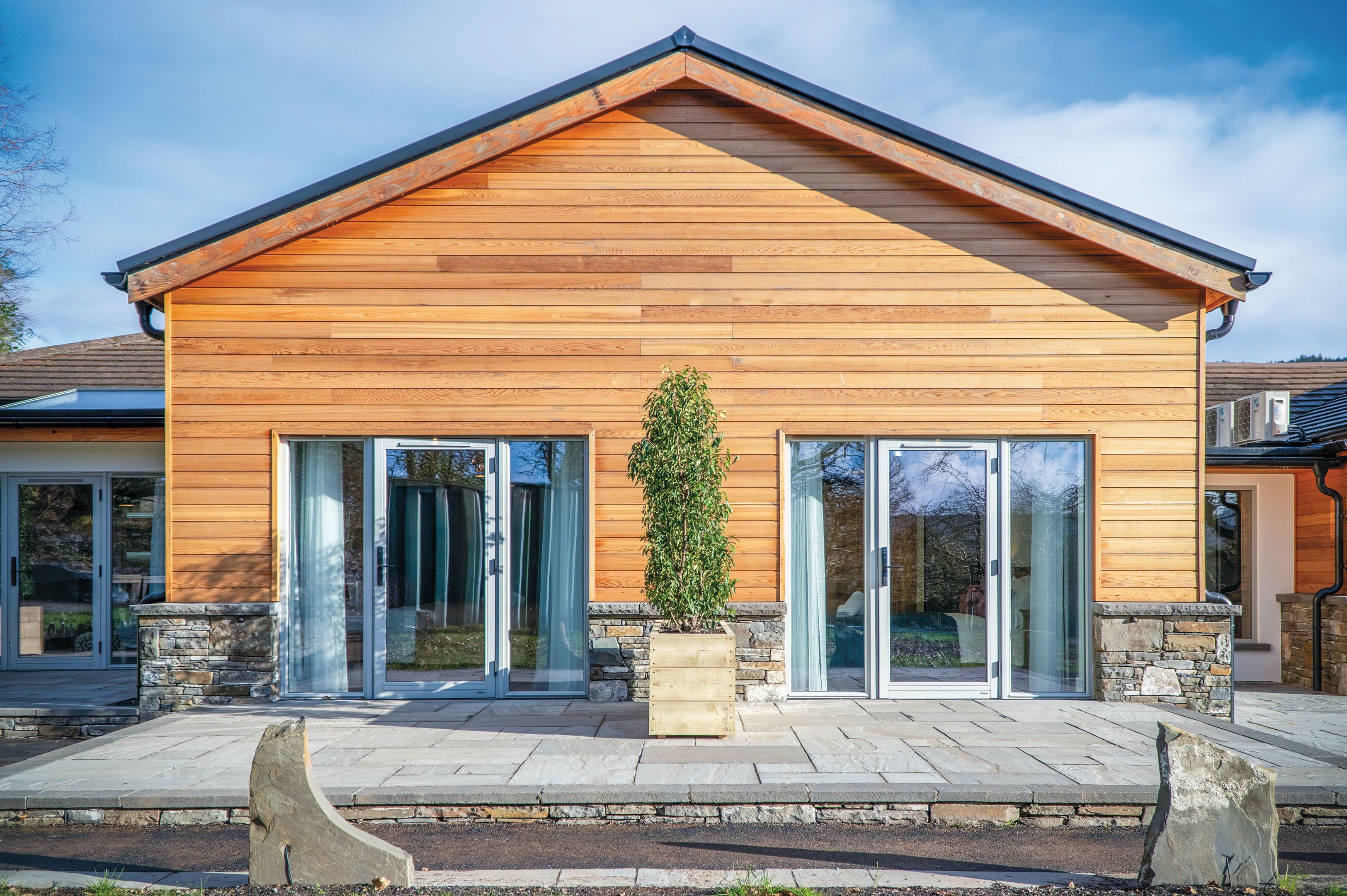 A modern wooden house with large glass doors and a stone foundation.