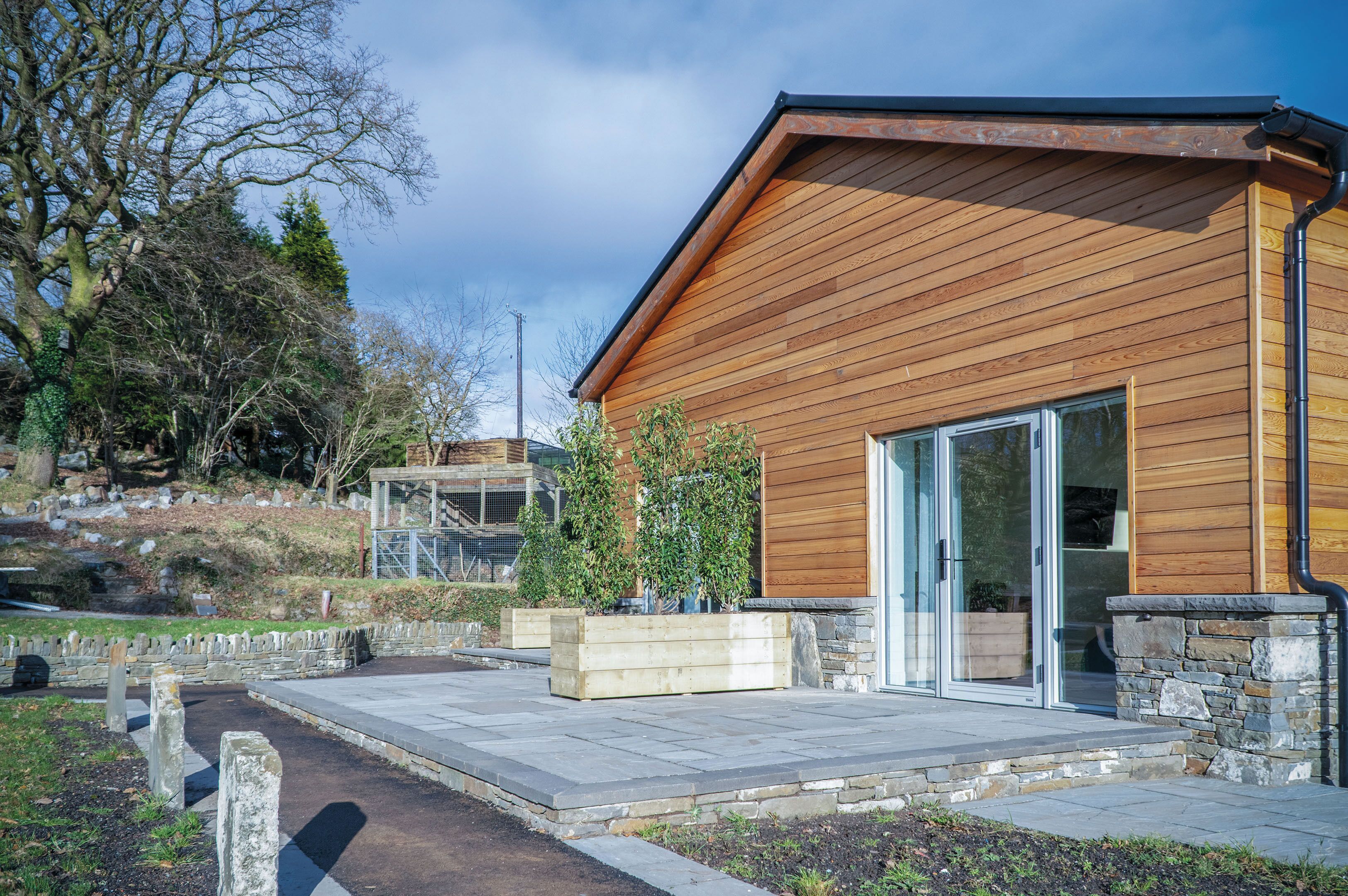 A modern building with wooden siding, a glass door entrance, and a stone foundation.