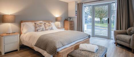 A modern bedroom with a large bed, bedside tables, a bench, and a view through a sliding glass door.