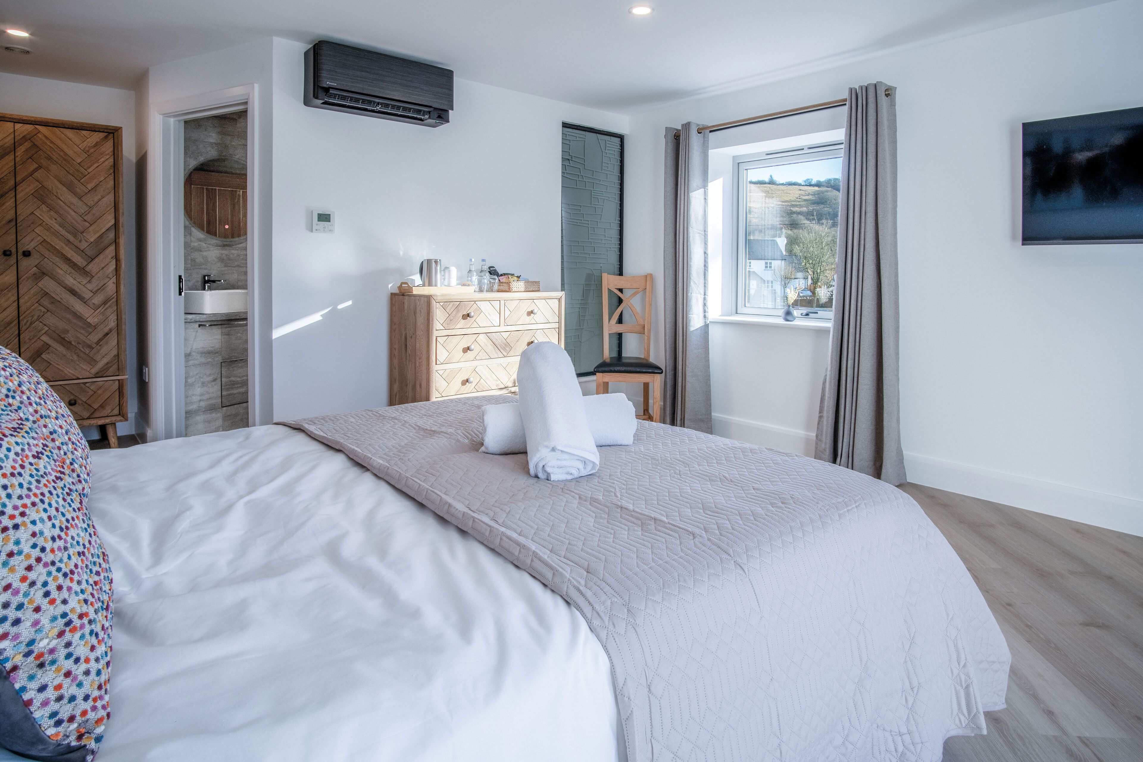 Une chambre à coucher avec un lit, une commode, une chaise et une fenêtre donnant sur un beau paysage.