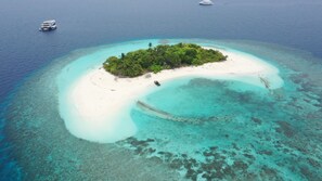 An aerial view of a small island with a white sandy beach, clear turquoise waters, and dense green vegetation. - Manta Sea View (Himandhoo)