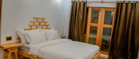 A wooden bed with a headboard made of stacked planks, a bedside table, and a window with curtains.