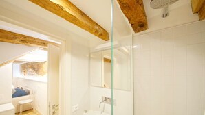Een moderne badkamer met een douchecabine van glas, witte tegels en zichtbare houten balken.