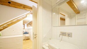 Een moderne badkamer met een wit wastafelmeubel, spiegel en houten balken aan het plafond.