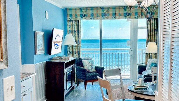 A room with a view of the ocean, a dining area with a table and chairs, a kitchen area, and a living area with a sofa and a chair. - Amazing Oceanfront Condo, Corner Unit, Natural Lights, 4th Floor (Myrtle Beach)