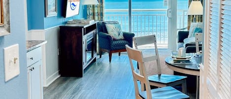 A room with a view of the ocean, a dining area with a table and chairs, a kitchen area, and a living area with a sofa and a chair.