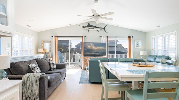 A spacious living room with a large window, a ceiling fan, and a dining area with a table and chairs.