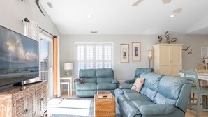 A living room with a large TV, a sectional sofa, a dining table, and a cabinet.