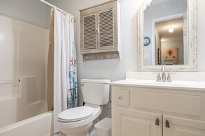 A bathroom with a toilet, a bathtub, a shower curtain, a sink with a mirror, and a cabinet. - Palm's Paradise, Oceanview Home located in Atlantic Beach, NC! (Atlantic Beach)