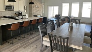 Une cuisine moderne dotée d’un îlot central, de tabourets de bar, d’une table à manger avec des chaises et d’un mur d’accent en pierre.