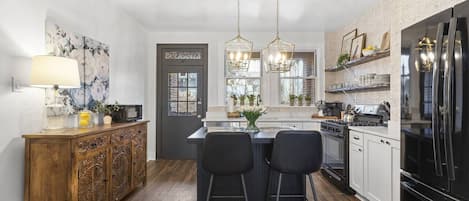 A modern kitchen with a central island, bar stools, a wooden cabinet, a refrigerator, and pendant lighting.