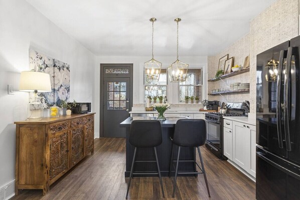 A modern kitchen with a central island, bar stools, a wooden cabinet, a refrigerator, and pendant lighting.