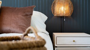 Un dormitorio con cama, mesita de noche, lámpara y pared con líneas verticales.