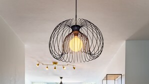 Un comedor con una mesa redonda de madera, sillas con cojines negros y una lámpara colgante negra de diseño.