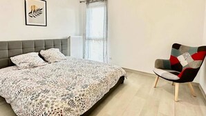 Quarto com cama, cadeira, radiador, janela com cortinas e quadro na parede.