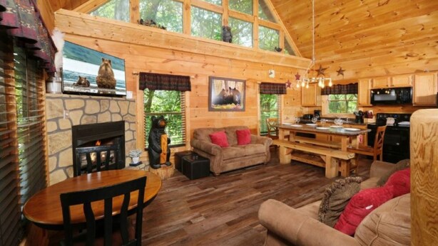 A cozy cabin interior with a stone fireplace, wooden walls, a dining area, and a kitchen. - Centrally Located between Pigeon Forge and Gatlinburg.  (Sevierville)