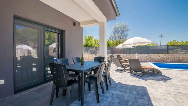 Une terrasse extérieure avec une table et des chaises, une piscine et un mur en pierre.
