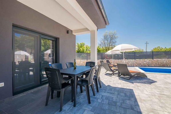 An outdoor patio with a table and chairs, a pool, and a stone wall.