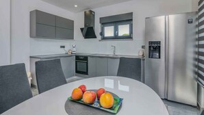 Une cuisine moderne avec des meubles gris, un réfrigérateur en acier inoxydable et une table à manger ornée de fruits.