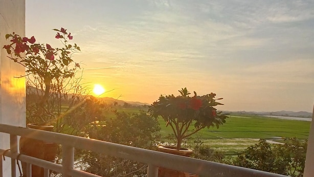 Ein Balkon mit Blick auf einen Sonnenuntergang über einer grünen Landschaft.